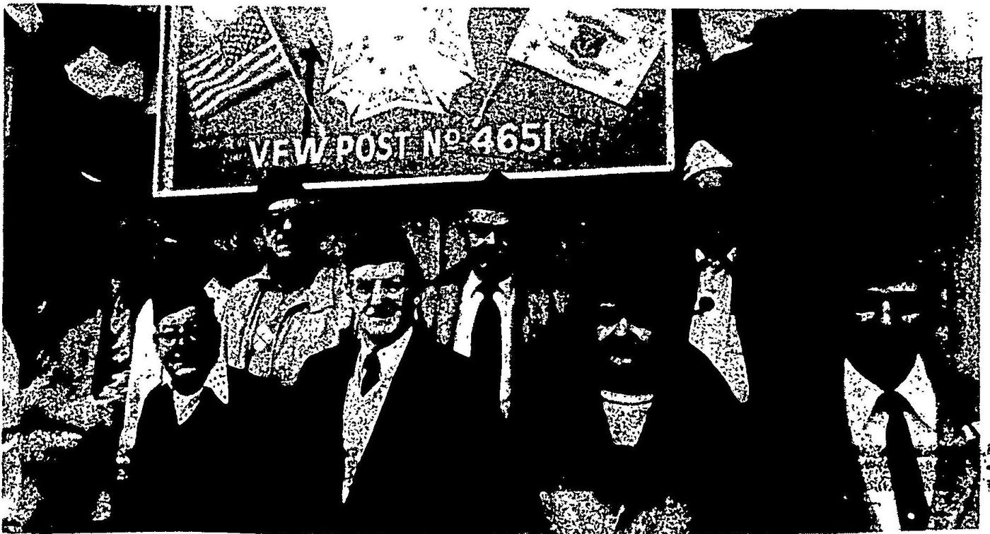 Nine members of VFW Post 4651, several in VFW caps, standing beneath the Post’s sign and flags at the 1986 dedication of 7 Haven Avenue.